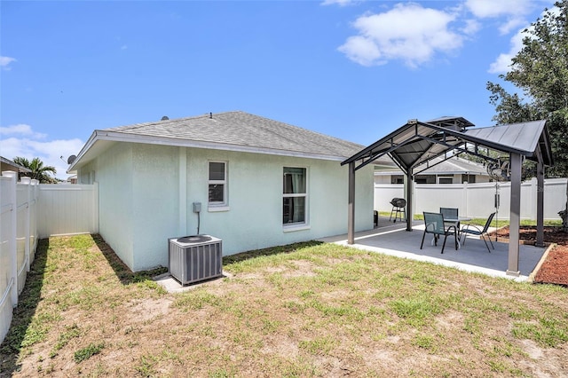 rear view of house featuring a gazebo, a patio area, central AC, stucco siding, and a shingled roof