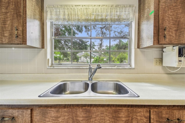 kitchen featuring a sink, light countertops, decorative backsplash, and brown cabinets