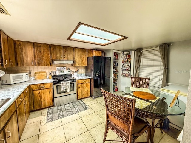 35058 Whispering Oaks Blvd, Dade City, FL 33523 - kitchen featuring stainless steel range with electric cooktop, black refrigerator with ice dispenser, under cabinet range hood, white microwave, and light countertops