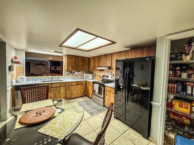 35058 Whispering Oaks Blvd, Dade City, FL 33523 - kitchen with black refrigerator with ice dispenser, stainless steel electric stove, a sink, white microwave, and brown cabinets