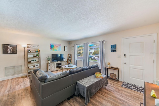 living room featuring light wood finished floors, a textured ceiling, and baseboards