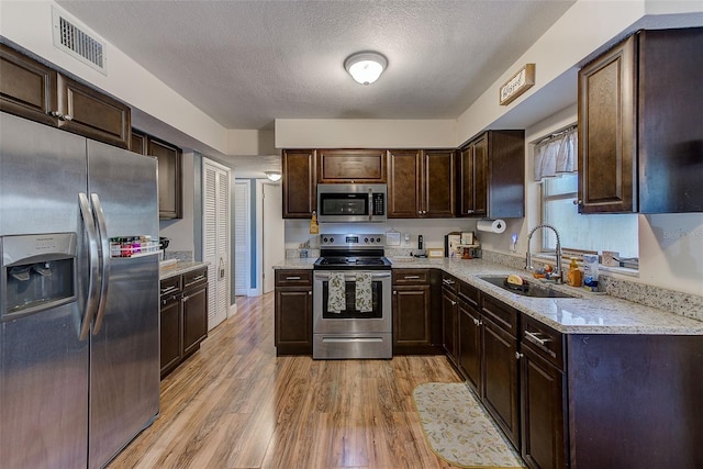 kitchen featuring appliances with stainless steel finishes, a sink, dark brown cabinets, light wood finished floors, and a textured ceiling