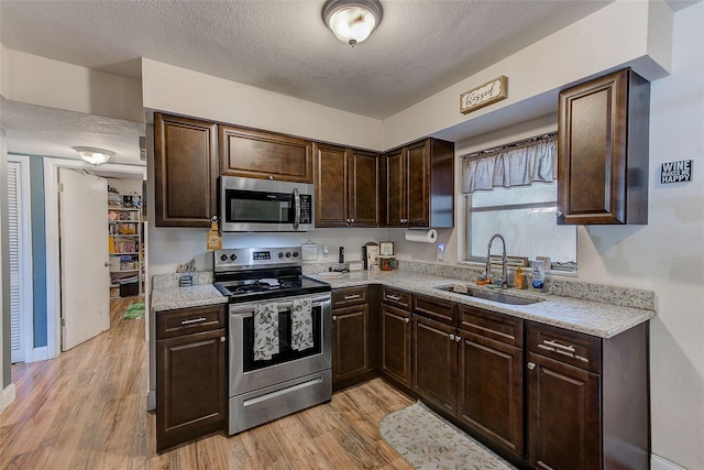 kitchen featuring appliances with stainless steel finishes, a sink, dark brown cabinets, light wood-type flooring, and a textured ceiling