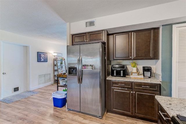 kitchen featuring stainless steel refrigerator with ice dispenser, dark brown cabinets, light wood-style floors, light stone counters, and baseboards