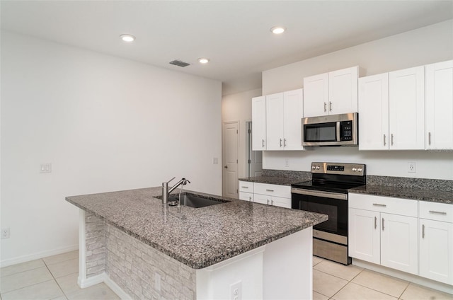 kitchen featuring appliances with stainless steel finishes, a sink, light tile patterned floors, dark stone counters, and white cabinetry