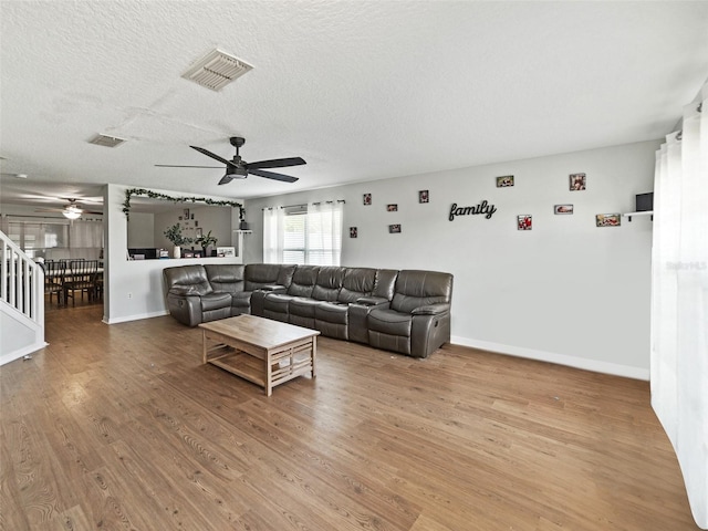 living area with a ceiling fan, wood finished floors, baseboards, and a textured ceiling