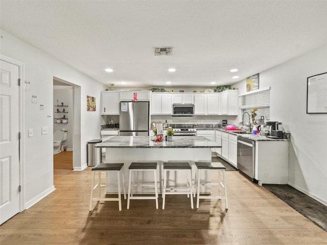 kitchen featuring appliances with stainless steel finishes, a center island, white cabinetry, a breakfast bar, and dark stone countertops