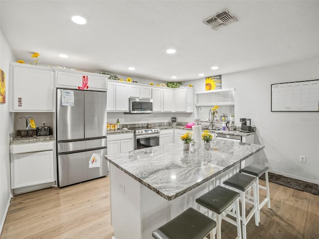 kitchen with stainless steel appliances, white cabinetry, light wood finished floors, a kitchen bar, and light stone counters