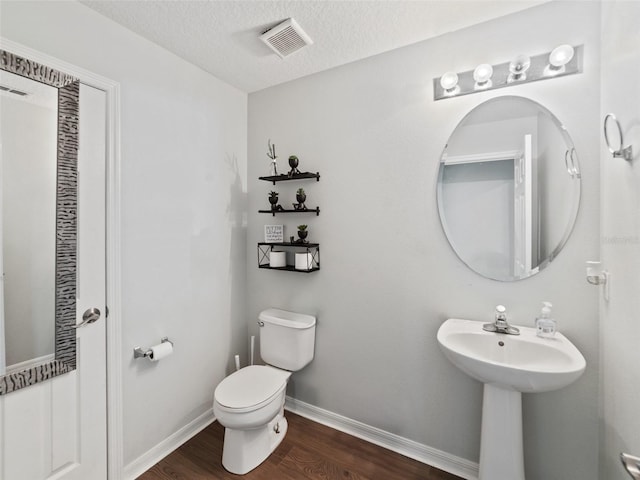 half bath with wood finished floors, toilet, baseboards, a textured ceiling, and a sink