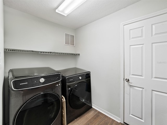 laundry area with washer and dryer, wood finished floors, baseboards, and a textured ceiling
