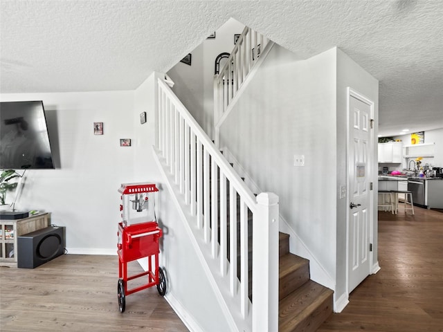 staircase with a textured ceiling, wood finished floors, and baseboards