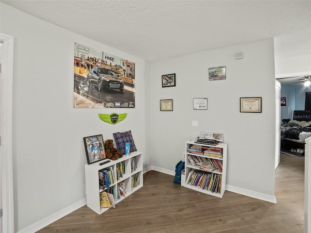 interior space with wood finished floors, baseboards, a ceiling fan, and a textured ceiling