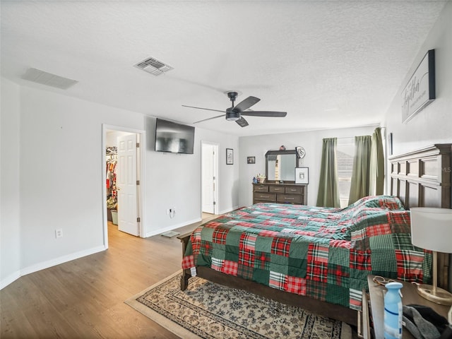 bedroom featuring wood finished floors, baseboards, a spacious closet, ceiling fan, and a textured ceiling