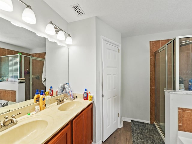 bathroom with a stall shower, double vanity, a bath, wood finished floors, and a textured ceiling