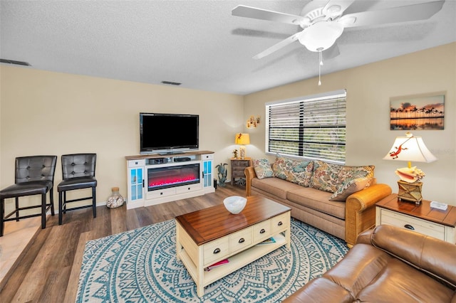 living area featuring wood finished floors, a textured ceiling, ceiling fan, and baseboards