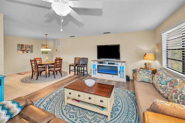 living area featuring wood finished floors, a textured ceiling, ceiling fan, and baseboards