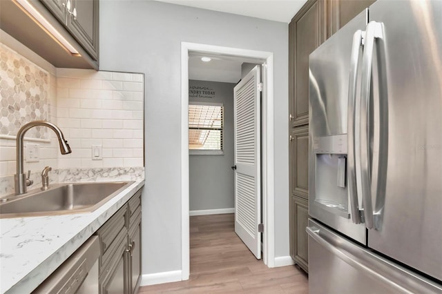 kitchen featuring stainless steel appliances, a sink, backsplash, light wood-style flooring, and baseboards