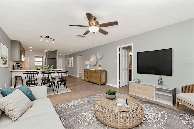 living area featuring light wood finished floors, ceiling fan, and baseboards