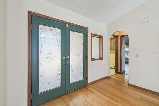 foyer with french doors, baseboards, arched walkways, and light wood-style floors