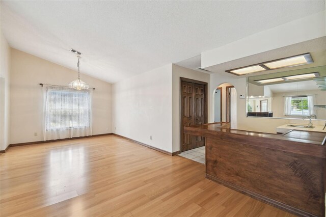 kitchen with arched walkways, a sink, light wood-style floors, vaulted ceiling, and pendant lighting
