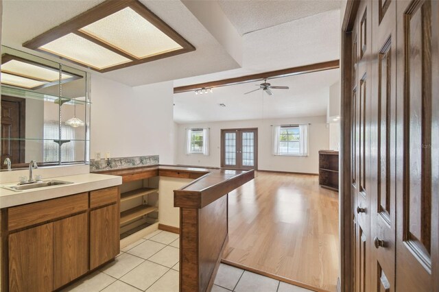 kitchen featuring a sink, a peninsula, brown cabinetry, a ceiling fan, and french doors