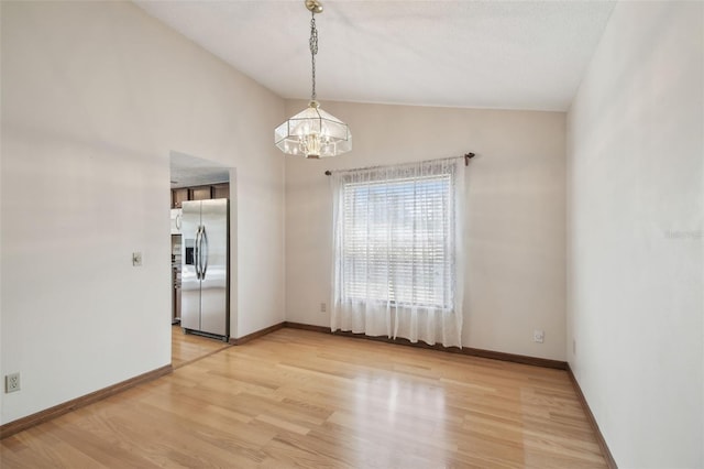empty room with a chandelier, light wood finished floors, lofted ceiling, and baseboards