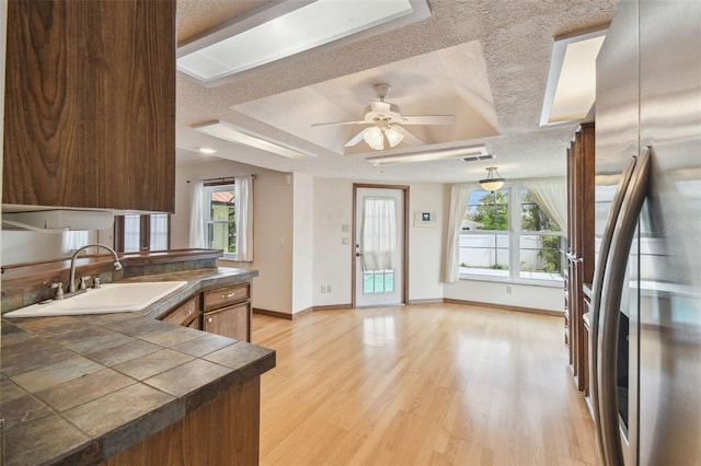 kitchen featuring stainless steel fridge, a sink, a textured ceiling, light wood finished floors, and healthy amount of natural light