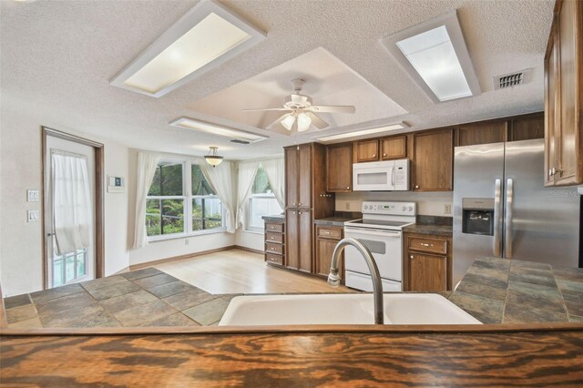 kitchen featuring white appliances, a textured ceiling, a sink, ceiling fan, and brown cabinetry