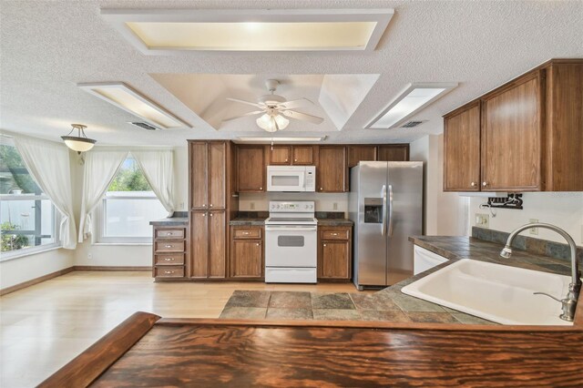 kitchen with white appliances, a sink, dark countertops, brown cabinetry, and a textured ceiling