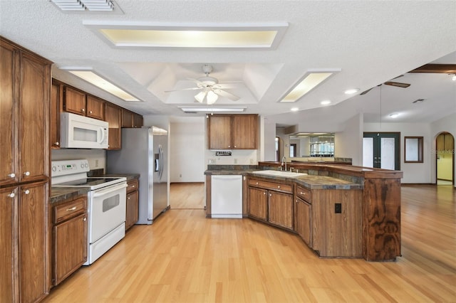kitchen featuring white appliances, a peninsula, dark countertops, a sink, and light wood finished floors