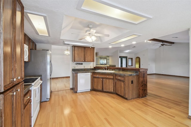 kitchen with white appliances, a ceiling fan, a peninsula, dark countertops, and a sink