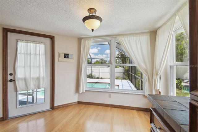 unfurnished dining area featuring a textured ceiling, light wood-style floors, healthy amount of natural light, and baseboards