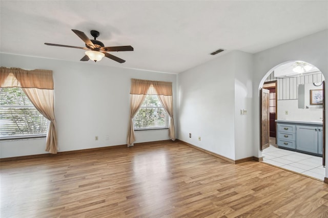 spare room featuring ceiling fan, light wood-style flooring, arched walkways, and baseboards