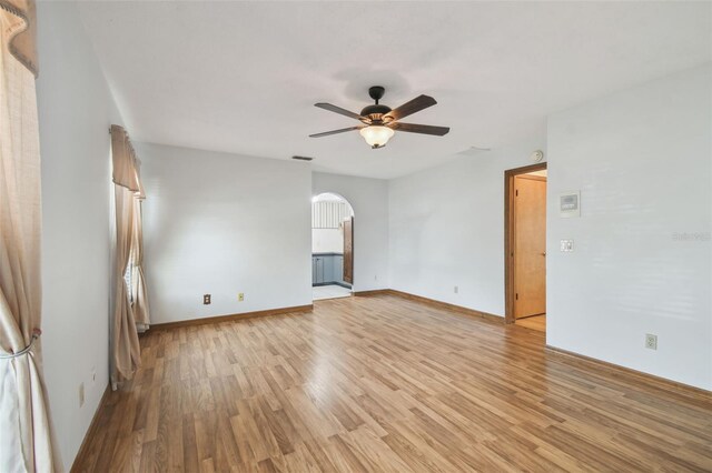 unfurnished room featuring a ceiling fan, light wood finished floors, arched walkways, and baseboards