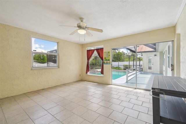 tiled empty room with a textured wall, healthy amount of natural light, ceiling fan, and a textured ceiling