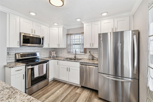 2018 21st St S, Saint Petersburg, FL 33712 - kitchen with appliances with stainless steel finishes, a sink, crown molding, white cabinetry, and light wood-type flooring