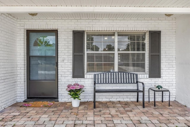 view of exterior entry featuring a porch and brick siding