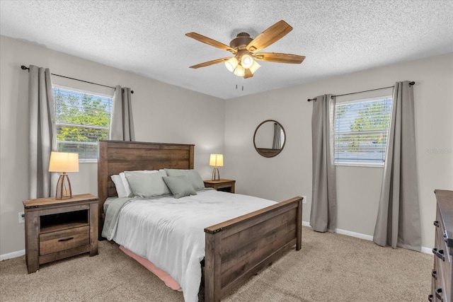 bedroom with multiple windows, light colored carpet, a textured ceiling, baseboards, and ceiling fan