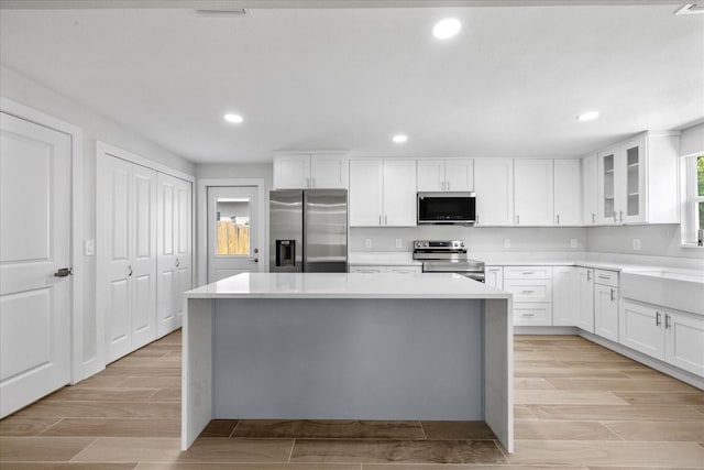 kitchen with stainless steel appliances, a kitchen island, glass insert cabinets, white cabinetry, and recessed lighting