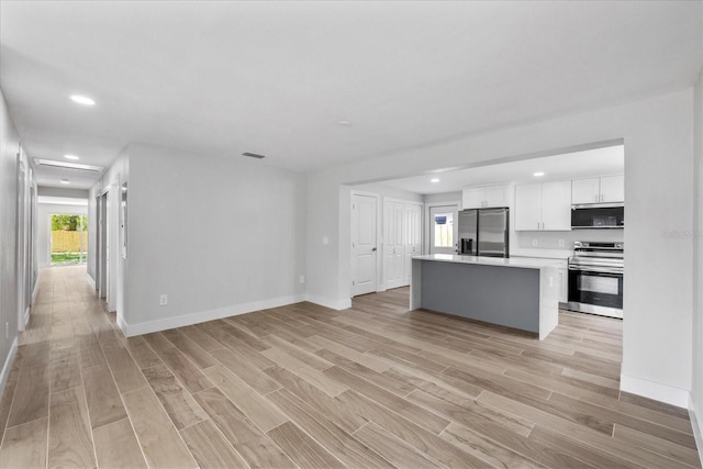 kitchen with appliances with stainless steel finishes, white cabinets, light wood-type flooring, light countertops, and open floor plan
