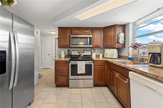 9126 Greenbriar Ln, Port Richey, FL 34668 - kitchen featuring appliances with stainless steel finishes, light tile patterned floors, a sink, brown cabinets, and light countertops