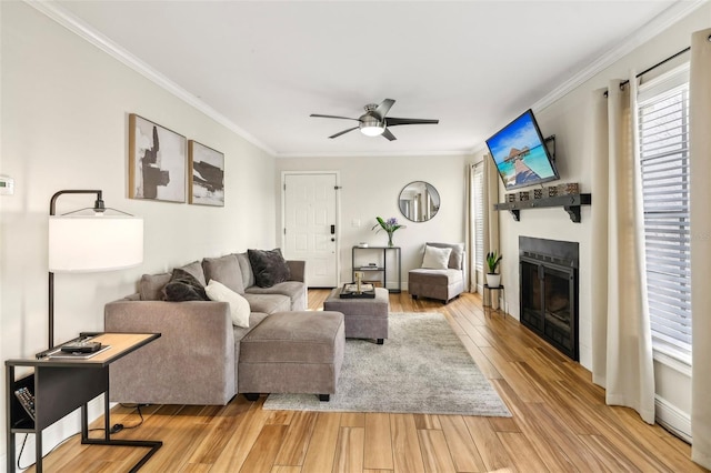 2969 Bonaventure Cir Unit 104, Palm Harbor, FL 34684 - living area with crown molding, a ceiling fan, a glass covered fireplace, light wood-style flooring, and baseboards