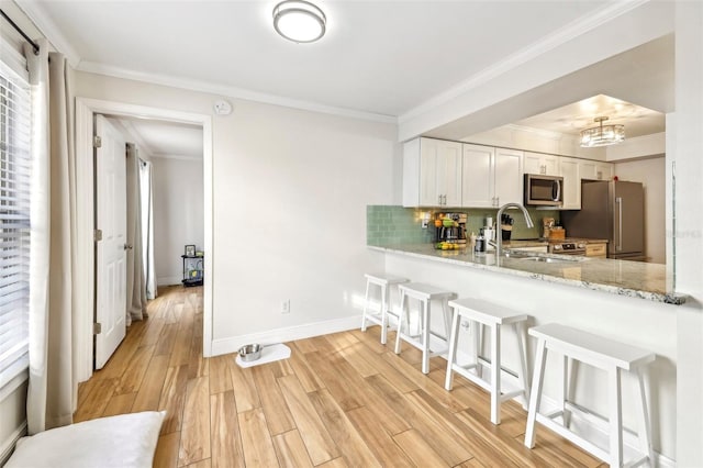 2969 Bonaventure Cir Unit 104, Palm Harbor, FL 34684 - kitchen featuring stainless steel appliances, light wood-type flooring, a kitchen bar, tasteful backsplash, and crown molding