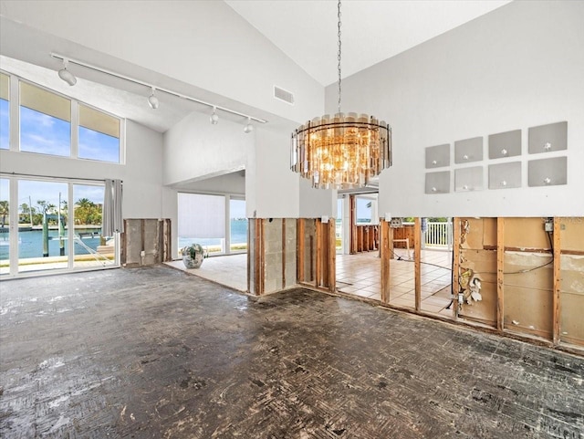 unfurnished living room featuring high vaulted ceiling, track lighting, a chandelier, and a water view