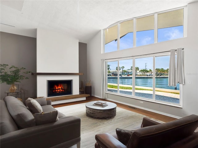 living room with a warm lit fireplace, baseboards, wood finished floors, high vaulted ceiling, and a textured ceiling