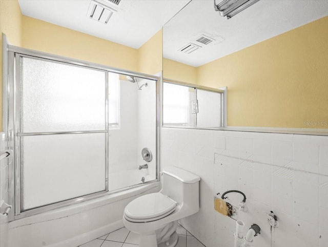 bathroom featuring tile walls, toilet, combined bath / shower with glass door, tile patterned floors, and wainscoting