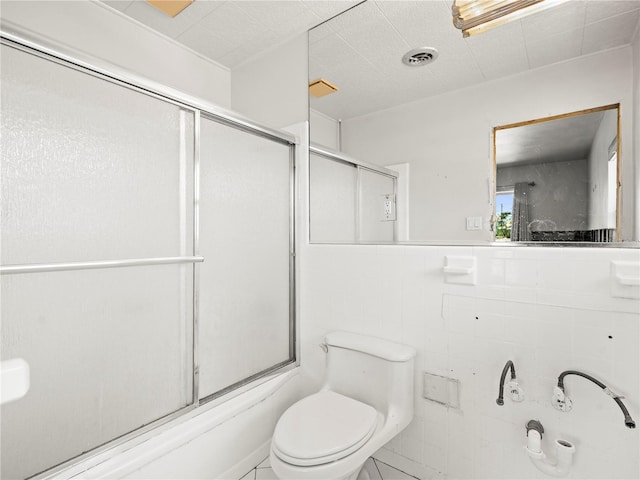 full bath featuring toilet, bath / shower combo with glass door, and tile walls