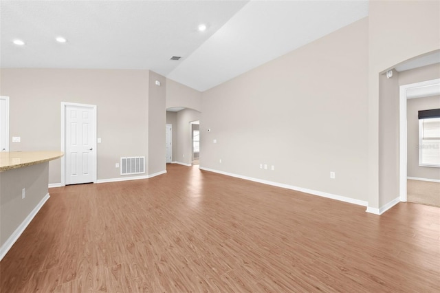 6937 Gideon Cir, Zephyrhills, FL 33541 - unfurnished living room with arched walkways, light wood-type flooring, baseboards, high vaulted ceiling, and recessed lighting