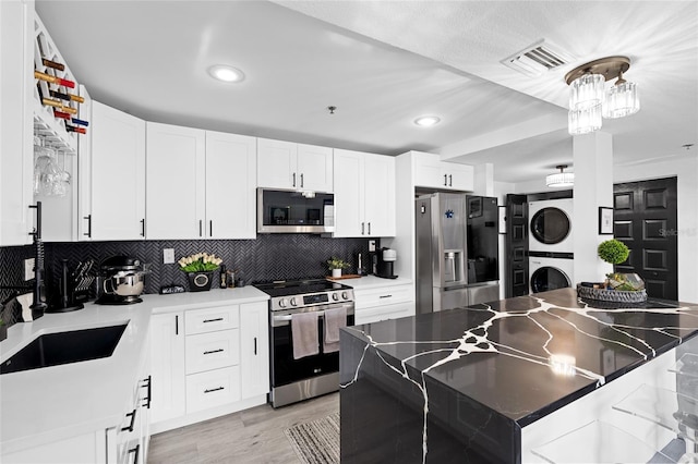 219 4th Ave N Unit 201, Saint Petersburg, FL 33701 - kitchen with stainless steel appliances, stacked washer and clothes dryer, decorative backsplash, white cabinets, and recessed lighting