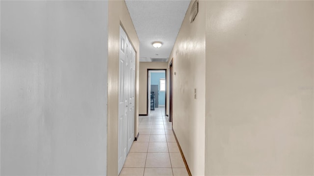 hallway with light tile patterned floors, baseboards, and a textured ceiling
